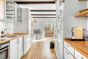 A modern kitchen with white cabinetry, wooden flooring, and a dining area with a table and chairs. - Thatched cottage with conservatory near beach (Græsted)