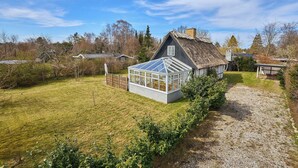 Une maison avec un toit de chaume, une véranda et une pelouse bien entretenue.