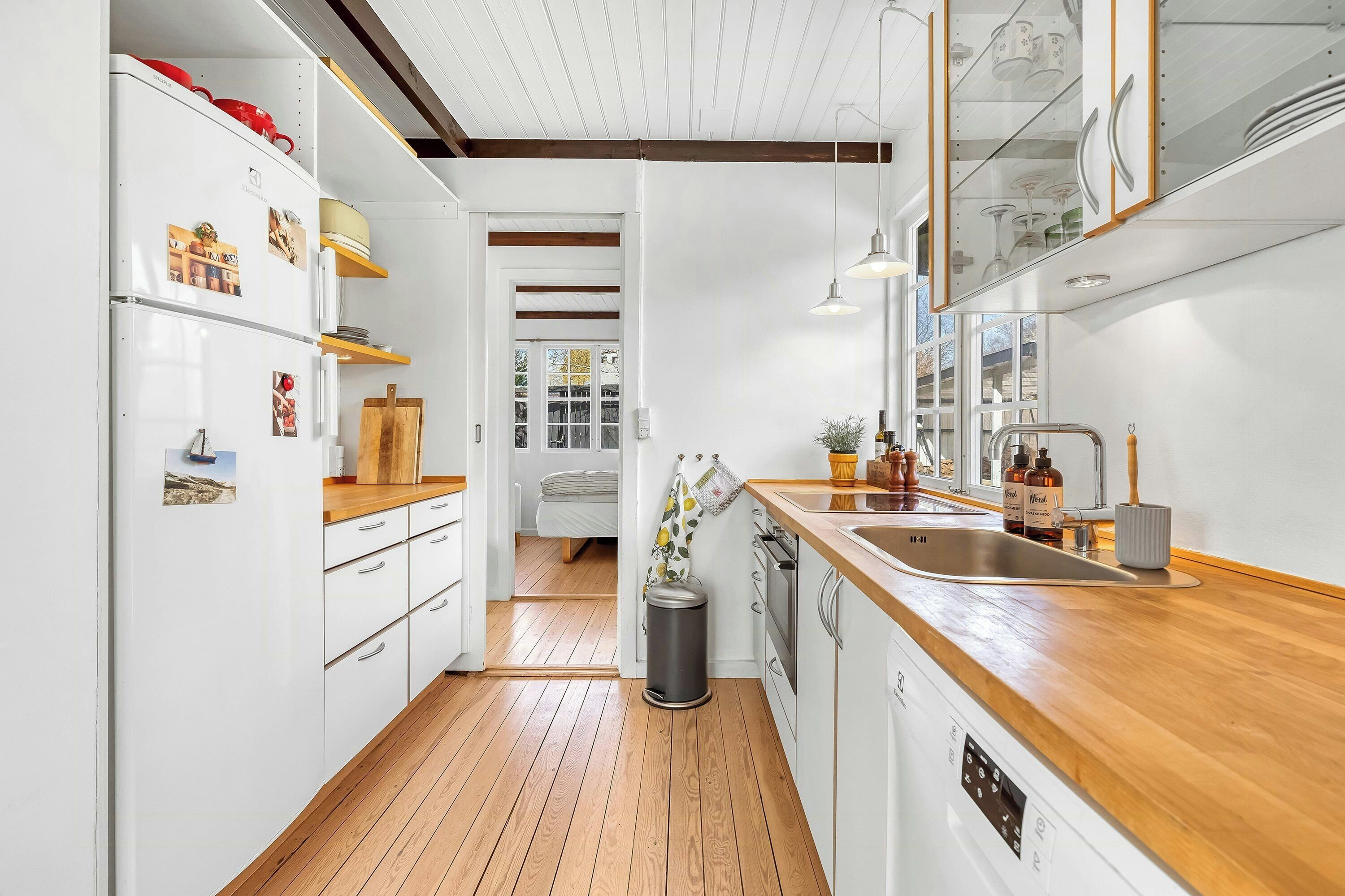 Una cocina moderna con armarios blancos, encimeras de madera, horno empotrado y un ventanal grande.