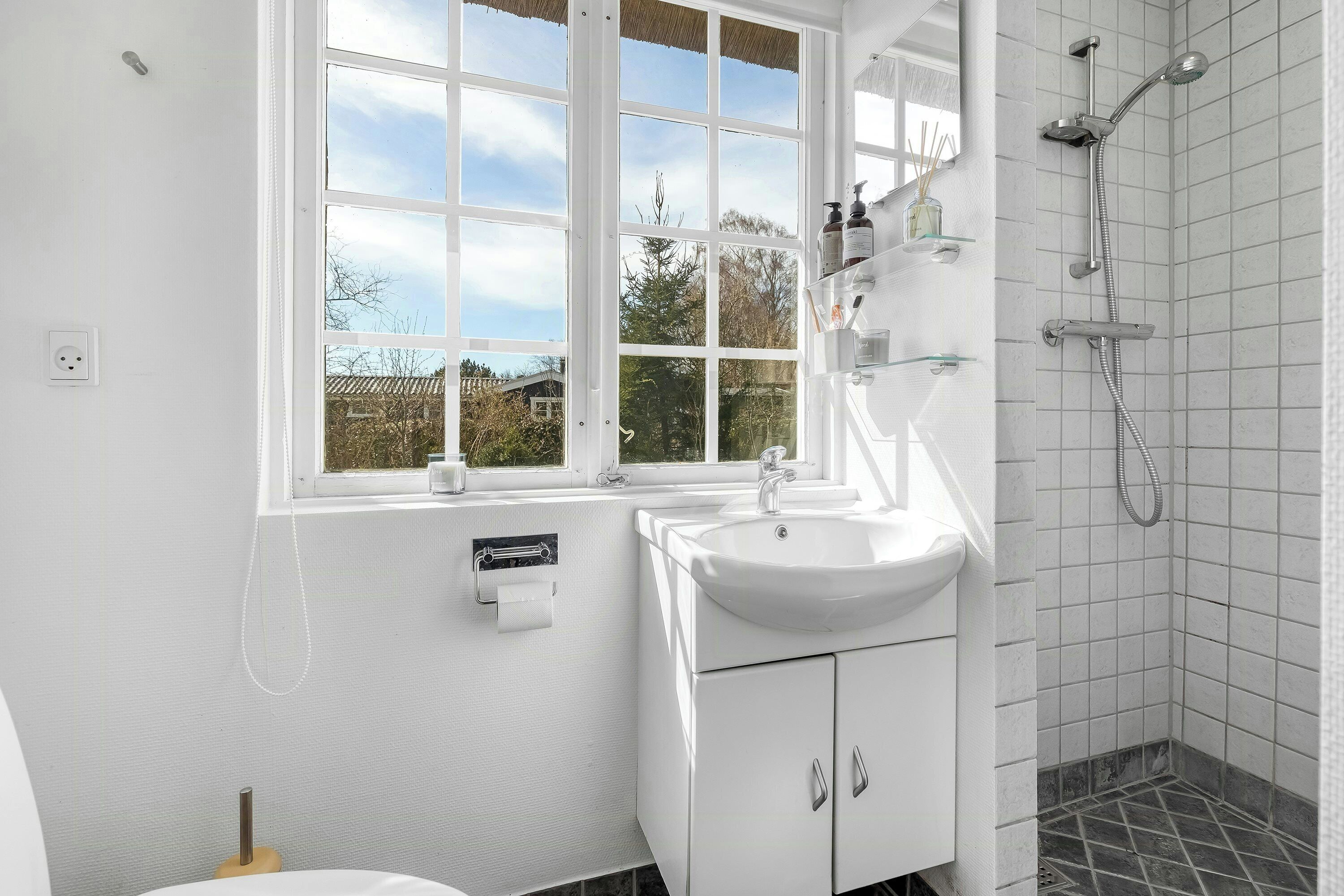 A bathroom with a window, a sink, a shower, and a toilet.