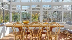 Une véranda avec une table et des chaises en bois, de grandes fenêtres et une vue sur les arbres.