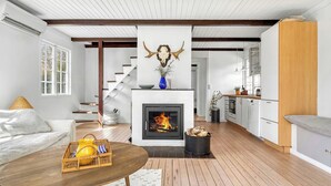 Un salon moderne avec une cheminée, un plancher en bois, un escalier et un coin cuisine.