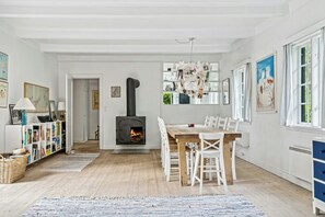 Ett mysigt vardagsrum med en öppen spis, en matplats med vita stolar och en bokhylla full av böcker.
