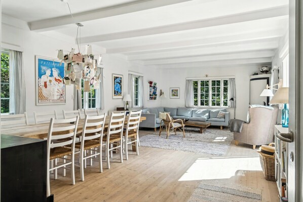 A spacious living area with a dining table, sofas, and a large window.