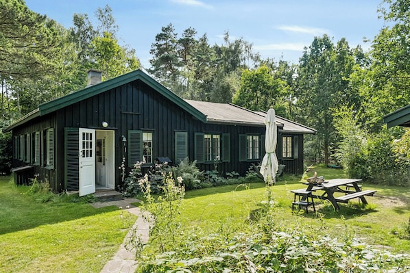 Eine rustikale Holzhütte mit grüner Tür, einem Picknicktisch und einem Garten.