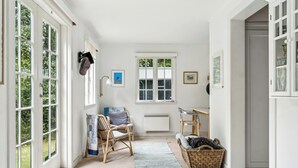 A room with large windows, wicker furniture, a radiator, and a door leading to another room. - Summer house with large nature plot in Rørvig (Rørvig)