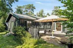 Eine Holzhütte mit einer Terrasse, einem überdachten Sitzbereich und einem Garten.