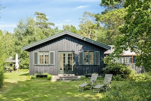 A wooden cabin with a porch, a lawn, and a chair.