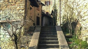 A stone staircase leading to a building with a stone facade and a window with red shutters.