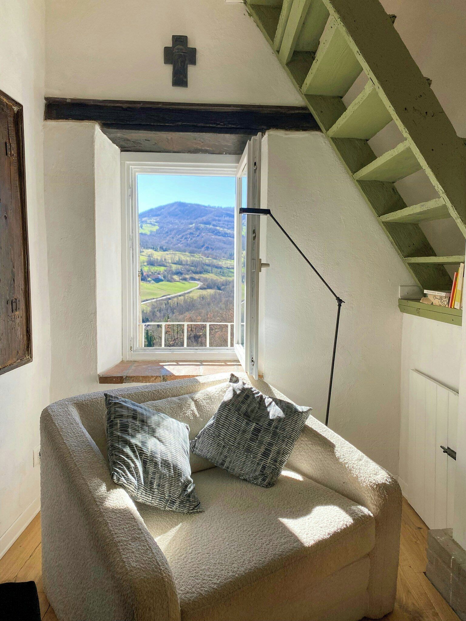 A cozy room with a sofa, pillows, a window with a view of the countryside, and a staircase.