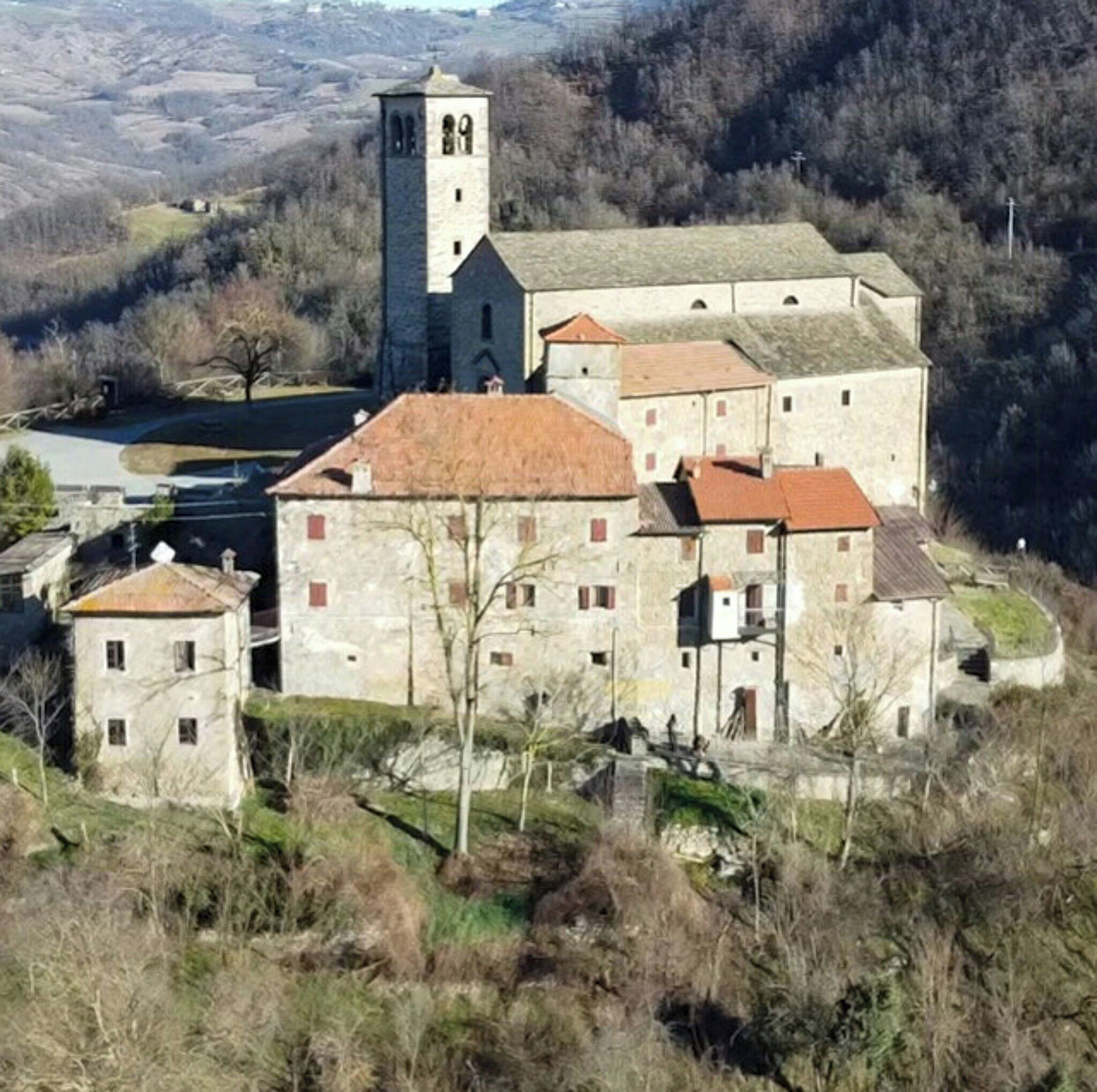 A historic stone building with a prominent tower, surrounded by a hilly landscape.