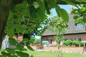 Ein Haus aus Ziegelsteinen mit einem Strohdach, einem kleinen Garten und einem Holzstuhl.