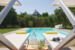 Ein Liegebereich am Pool mit einer Flasche, Gläsern und Sonnenbrillen auf einem Tablett.