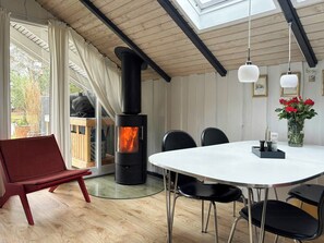 A modern interior with a round table, black chairs, a red bench, a black wood-burning stove, and a skylight. - Summer house on natural plot with three terraces (Ebeltoft)