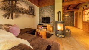 A cozy living room with a fireplace, a television, and a painting of trees on the wall. - Chalet with sauna at Ilsetal in the Harz (Ilsenburg (Harz))