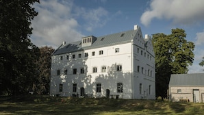 A large, white building with multiple windows and a sloped roof, surrounded by a grassy area and trees. - Spacious holiday apartment on Rügen (Poseritz)