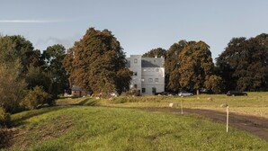 A multi-story building with a flat roof, surrounded by trees and a grassy field. - Spacious holiday apartment on Rügen (Poseritz)
