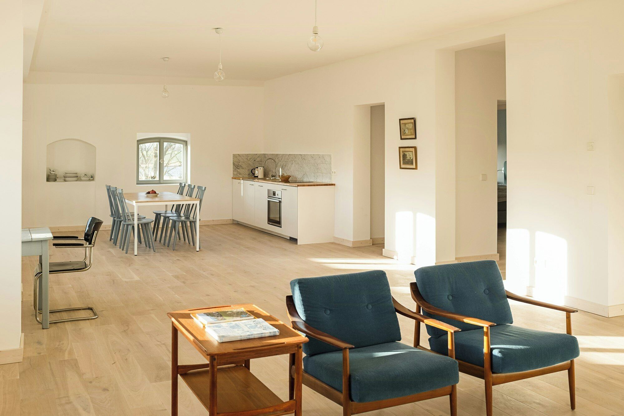 Een ruime woonkamer met een eettafel, stoelen, een bank en een keuken op de achtergrond.