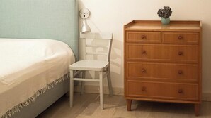 A bedroom with a bed, a wooden dresser, a chair, and a wall-mounted lamp. - Spacious holiday apartment on Rügen (Poseritz)