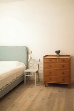 Ein Schlafzimmer mit einem Bett, einem Holzschrank, einem Sessel und einer Wandlampe.