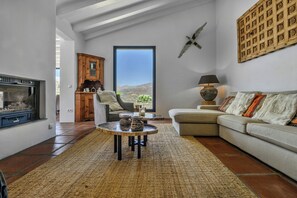Ein Wohnzimmer mit Kamin, einer Couch, einem Couchtisch und Blick durch ein großes Fenster.