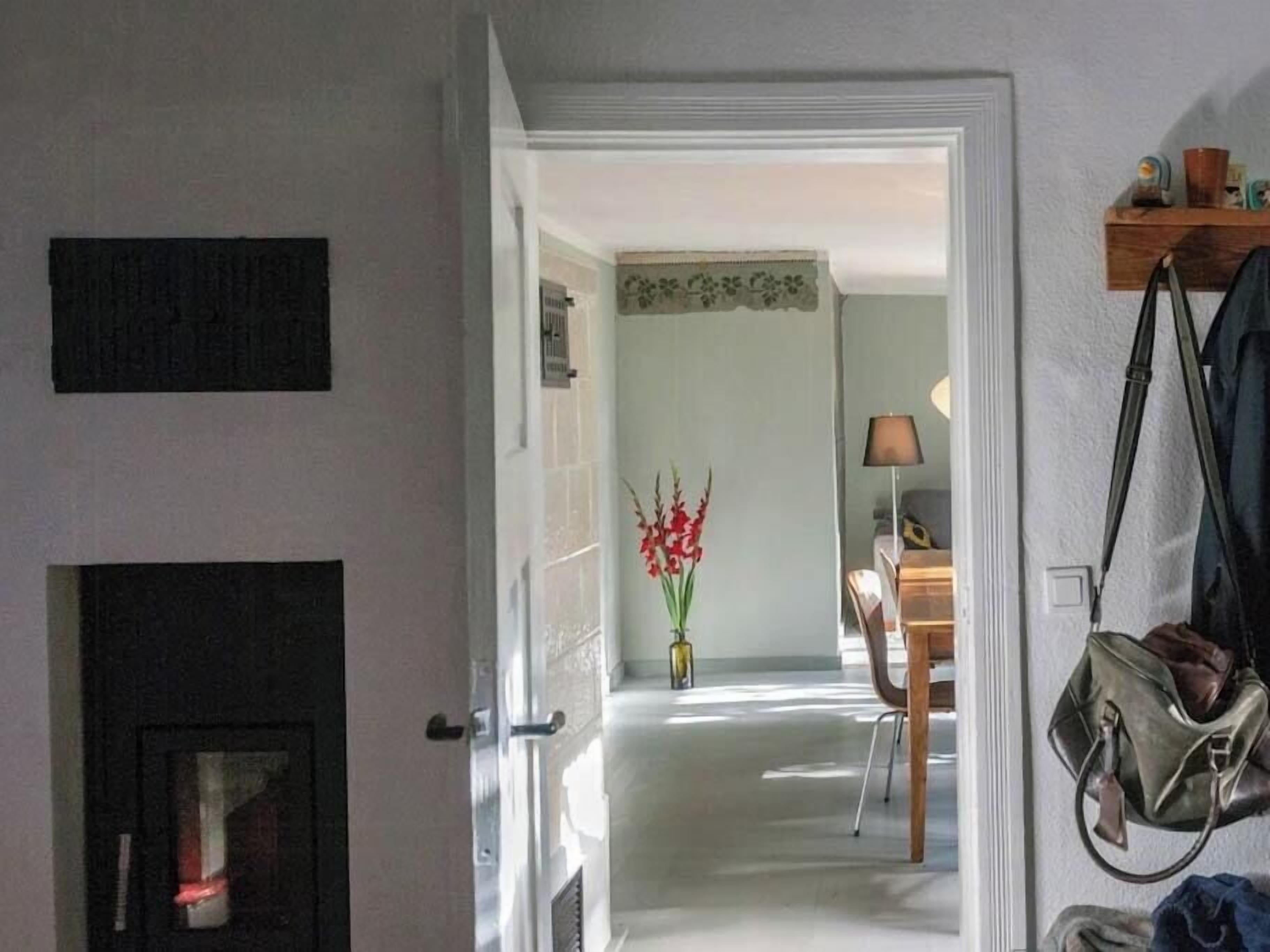 Ein Flur mit einer zurueckliegenden Tür, einer Blumenvase, einem Schreibtisch mit Lampe und einer überkünglichen Tasche.