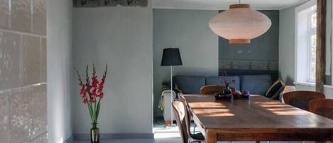 A dining area with a wooden table, wicker chairs, a vase with red flowers, and a hanging light fixture.