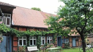 Et hus med tegltag, en have med bænk og bord, samt et træ.