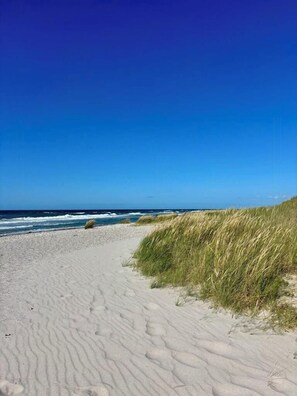 Ein Sandstrand mit Wellen, blauem Himmel und Dünen.