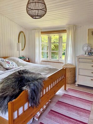 Ein Schlafzimmer mit einem hölzernen Bett, einer Nachttischlampe, einem Spiegel, einem Schminktisch und einem Fenster mit Vorhängen.