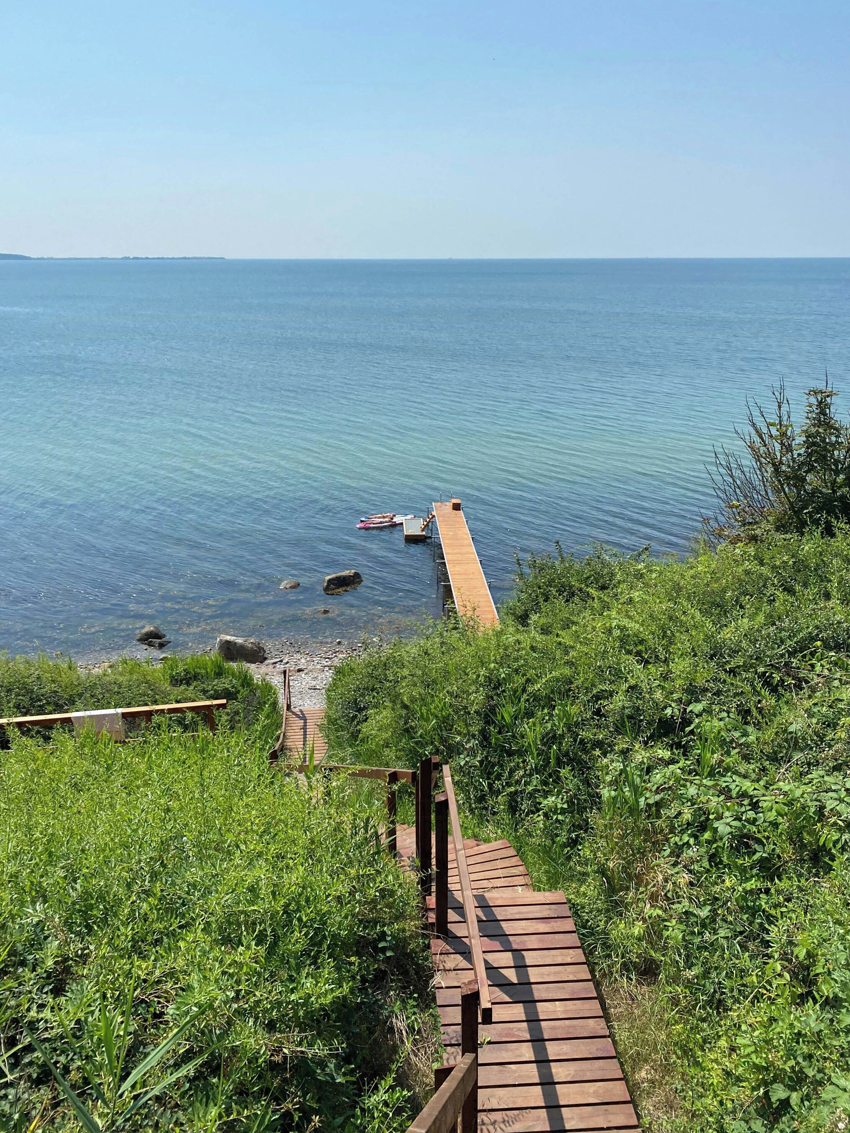 A wooden boardwalk leading to a rocky shoreline with clear blue water.