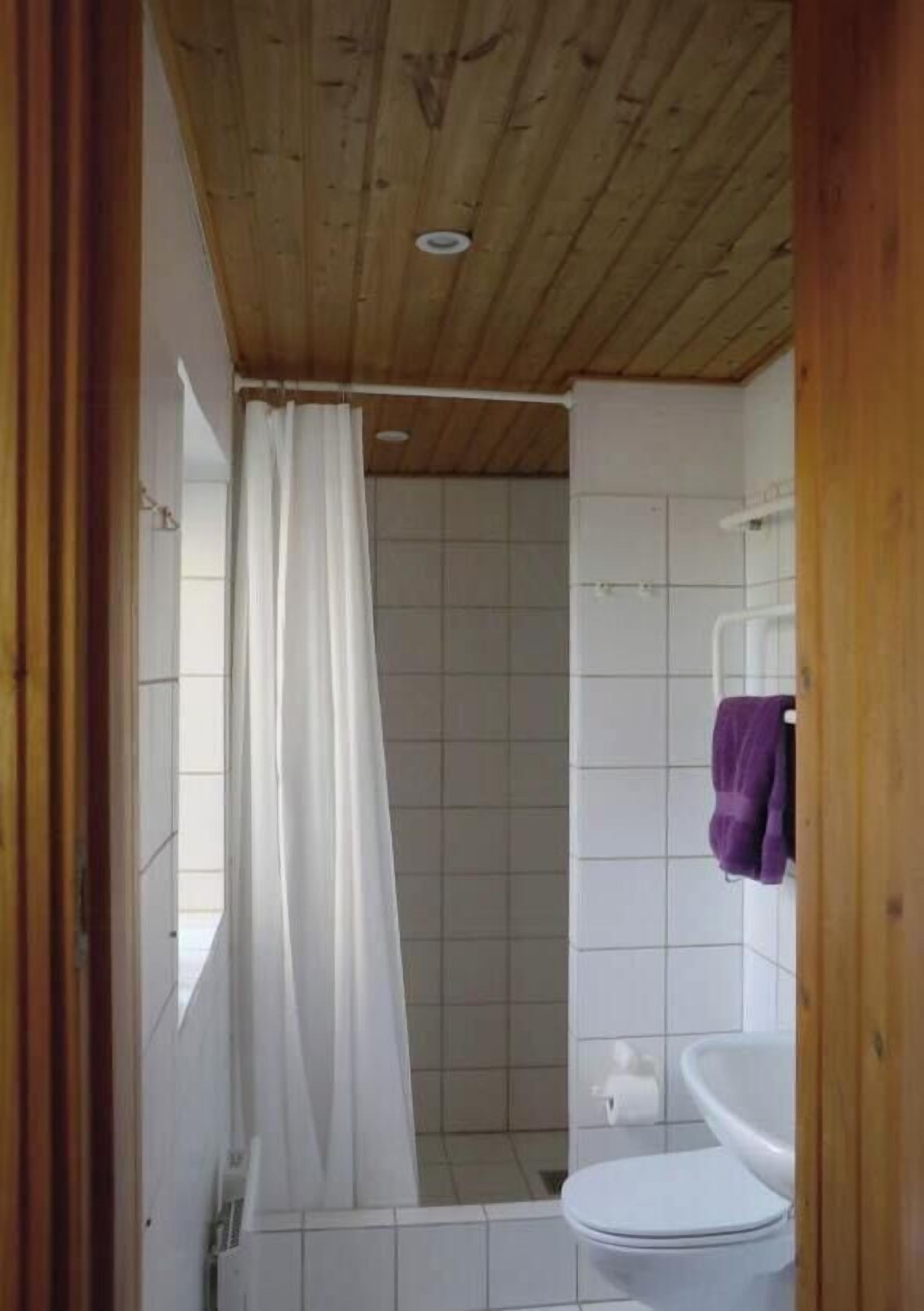 Un baño con ducha, inodoro y techo de madera.