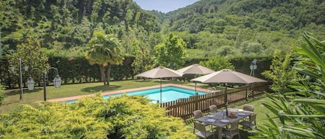 Una piscina rodeada por una valla de madera, con asientos al aire libre y sombrillas.