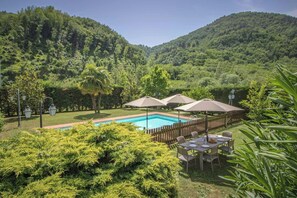 Ein Pool, umgeben von einem Holzzaun, mit Gartenmöbeln und Sonnenschirmen.