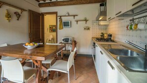 Een keuken met een houten tafel, witte stoelen, een magnetron en een spoelbak.