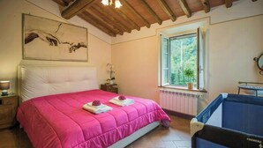 Een slaapkamer met een groot bed, een raam met uitzicht, een houten plafond en een klein nachtkastje met een lamp.