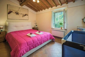 Ein Schlafzimmer mit einem großen Bett, einem Fenster mit Aussicht, einer Holzbalkendecke und einem kleinen Nachttisch mit Lampe.