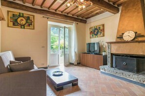 Ein Wohnzimmer mit einer Couch, einem Couchtisch, einem Kamin, einem Fernseher und einer Tür, die nach draußen führt.