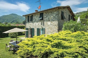 Ein Steinhaus mit grünen Fensterläden, einem Tisch mit Stühlen und einem Garten davor.