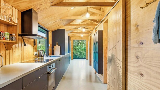 Une cuisine moderne avec des poutres en bois, un long plan de travail et une vue sur la verdure environnante.