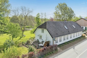 Ett vitt hus med ett sluttande tak, en inhägnad trädgård och en blomsterträdgård.