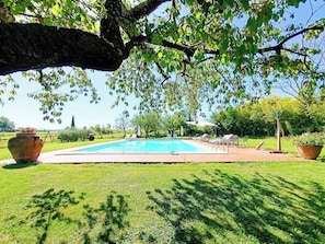 A swimming pool surrounded by grass, with trees and outdoor furniture. - Villa in the farmhouse with pool in Tuscany (Bucine)