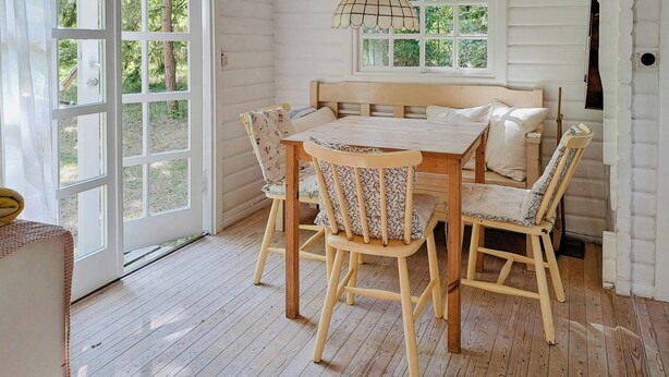 A room with a wooden table and chairs, a hanging light fixture, and large windows with a view of greenery. - Retro and simplicity in two small houses by Arresø (Frederiksværk)