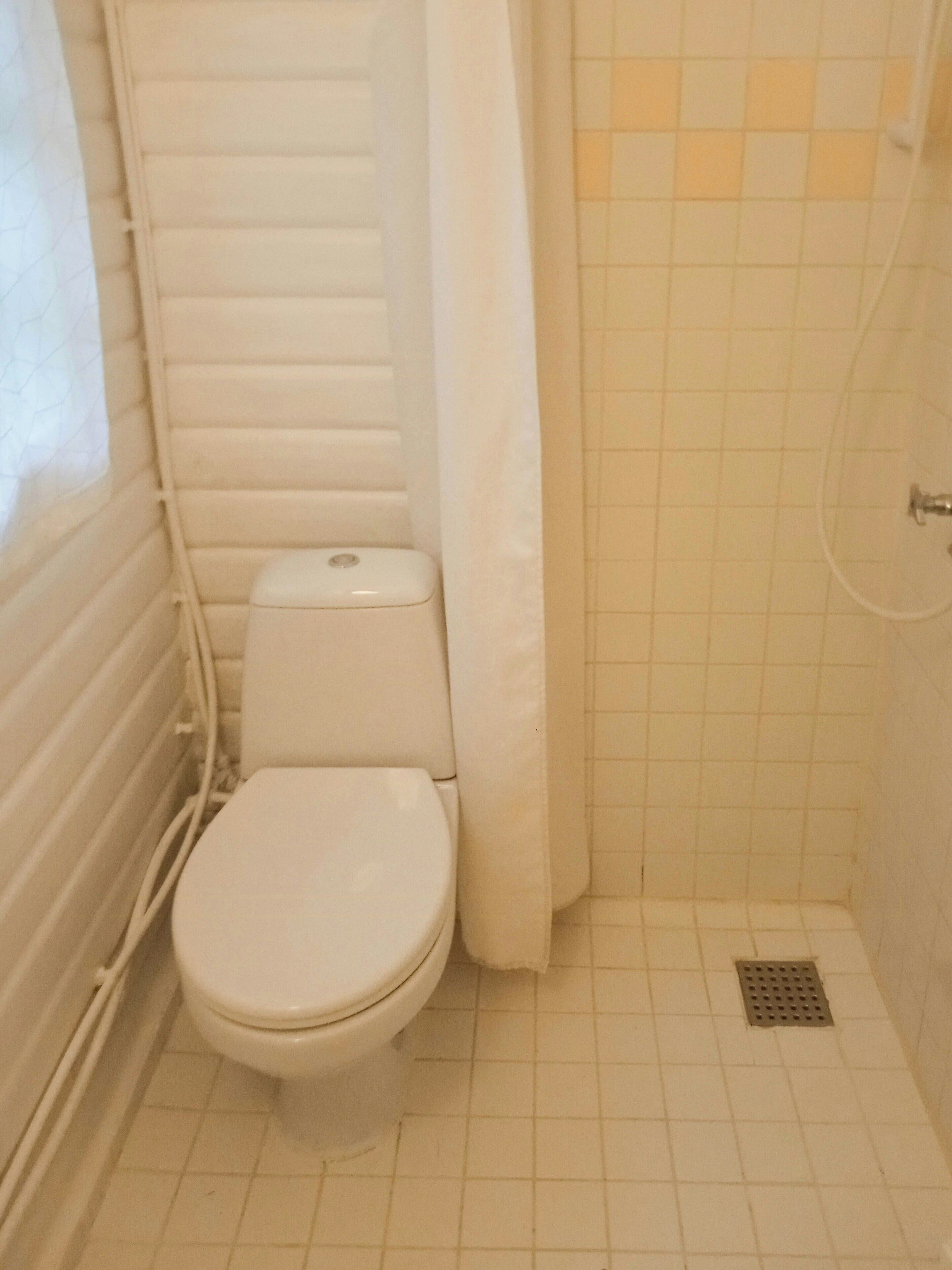 Ein kleines, kompaktes Badezimmer mit Toilette, Duschbereich und Fliesenboden.