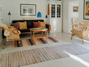 Een woonkamer met een bank, twee fauteuils, een salontafel, een gestreept vloerkleed, een kast en een schilderij aan de muur.