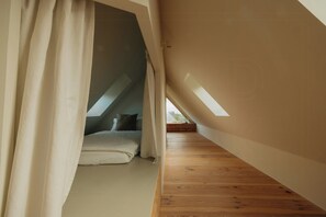 Ein Schlafzimmer mit schrägen Wänden, einem Bett mit Kissen und Holzboden.