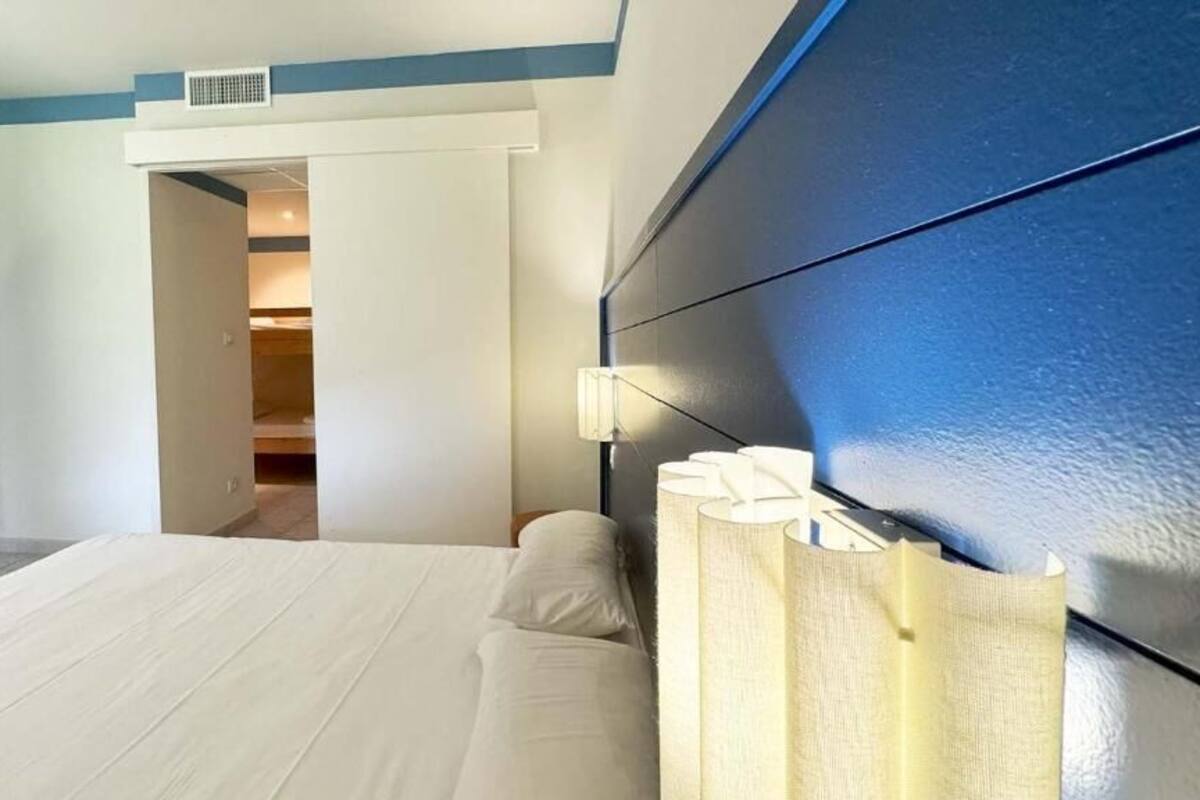 A bedroom with a bed, a bedside table, a nightstand, and a door leading to another room.