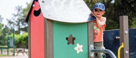 Niño trepando una estructura de parque infantil con una combinación de colores verde, rojo y marrón.