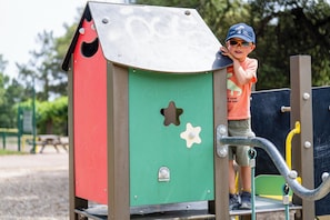 A child climbing a playground structure with a green, red, and brown color scheme.