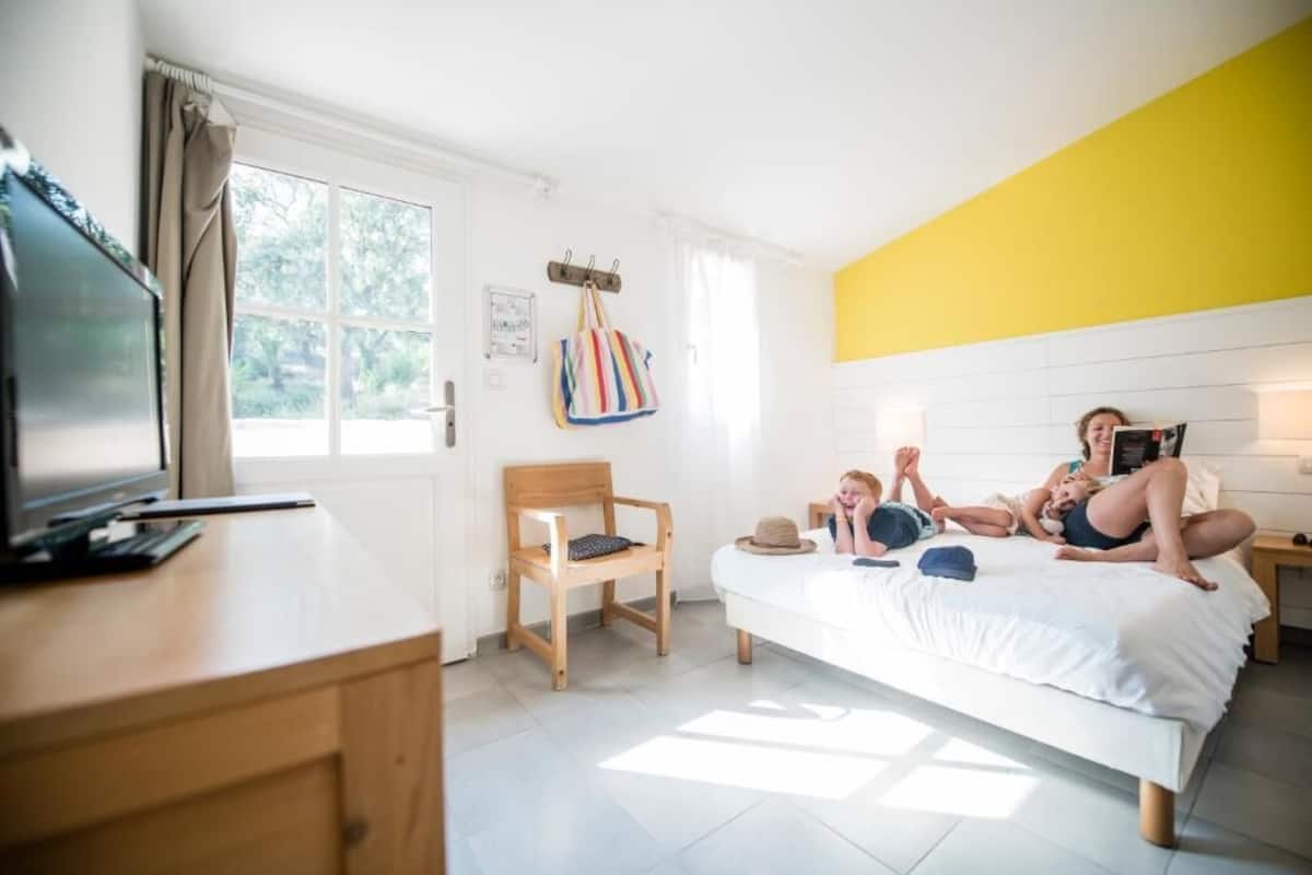 A bedroom with a bed, a desk, a chair, a television, and a window.